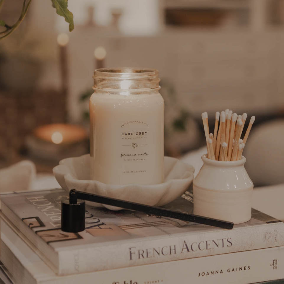 A Mason Jar Candle labeled 'Earl Grey'  set on a book, with a decorative jar of matches next to it.