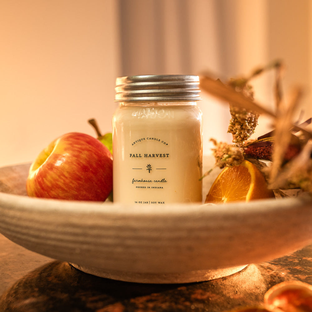 Candle labeled 'Fall Harvest' on a decorative plate with apples and pinecones.